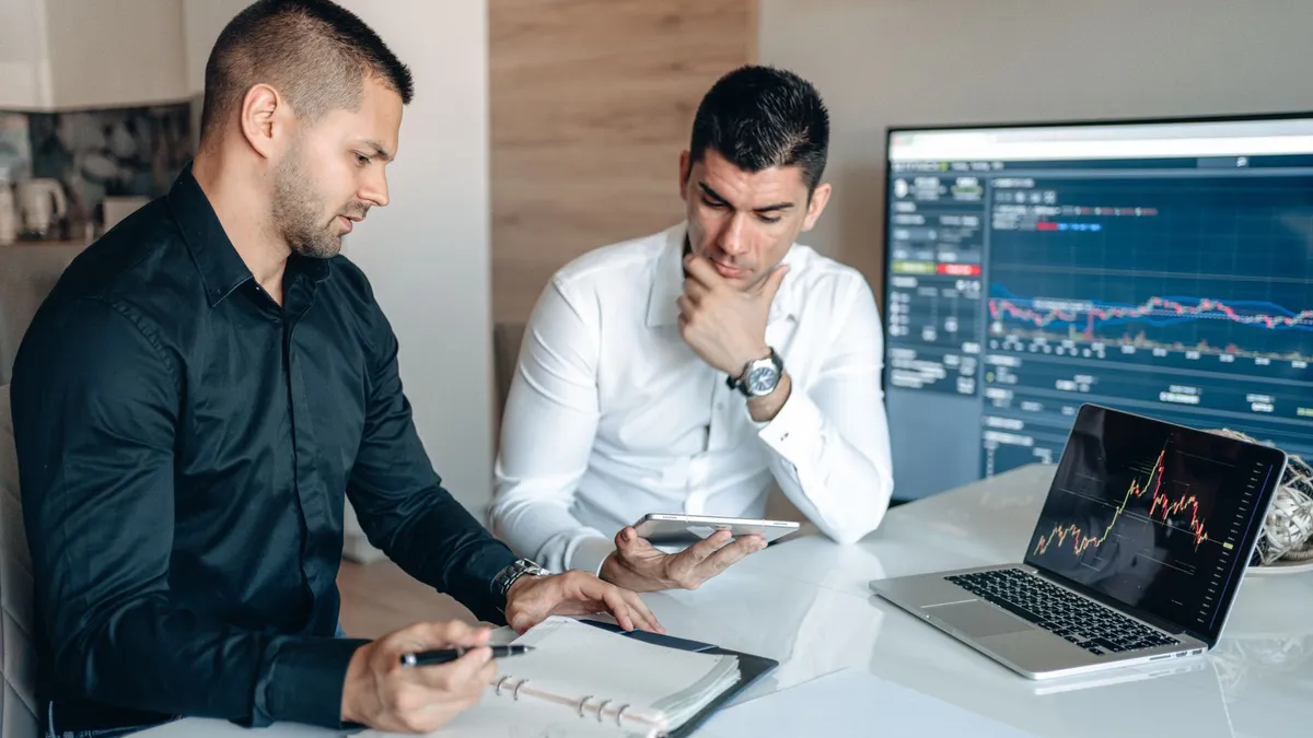 Two businessmen discussing stock market analytics in a modern office setting.