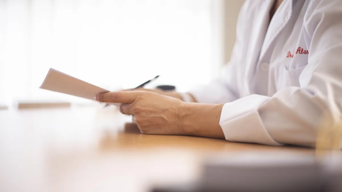Close-up of a doctor in a lab coat reviewing paperwork at a desk.