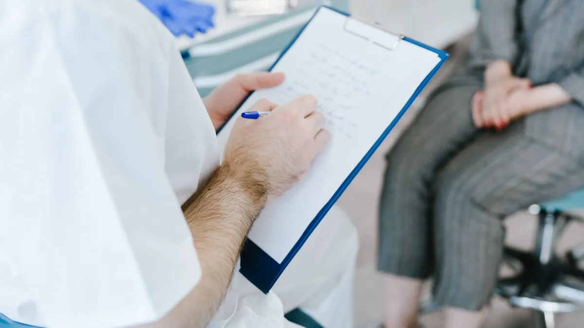 Medical professional writing patient notes on clipboard during consultation.