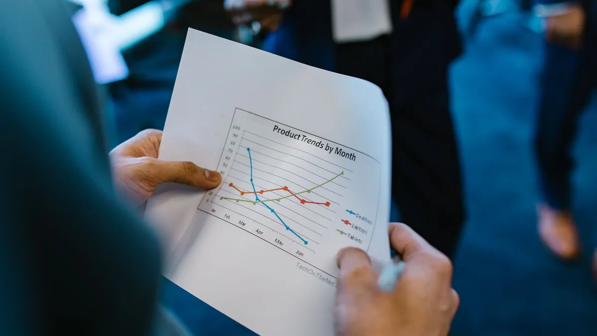 Close-up of hands holding a paper with a line graph showing product trends by month during a business meeting.
