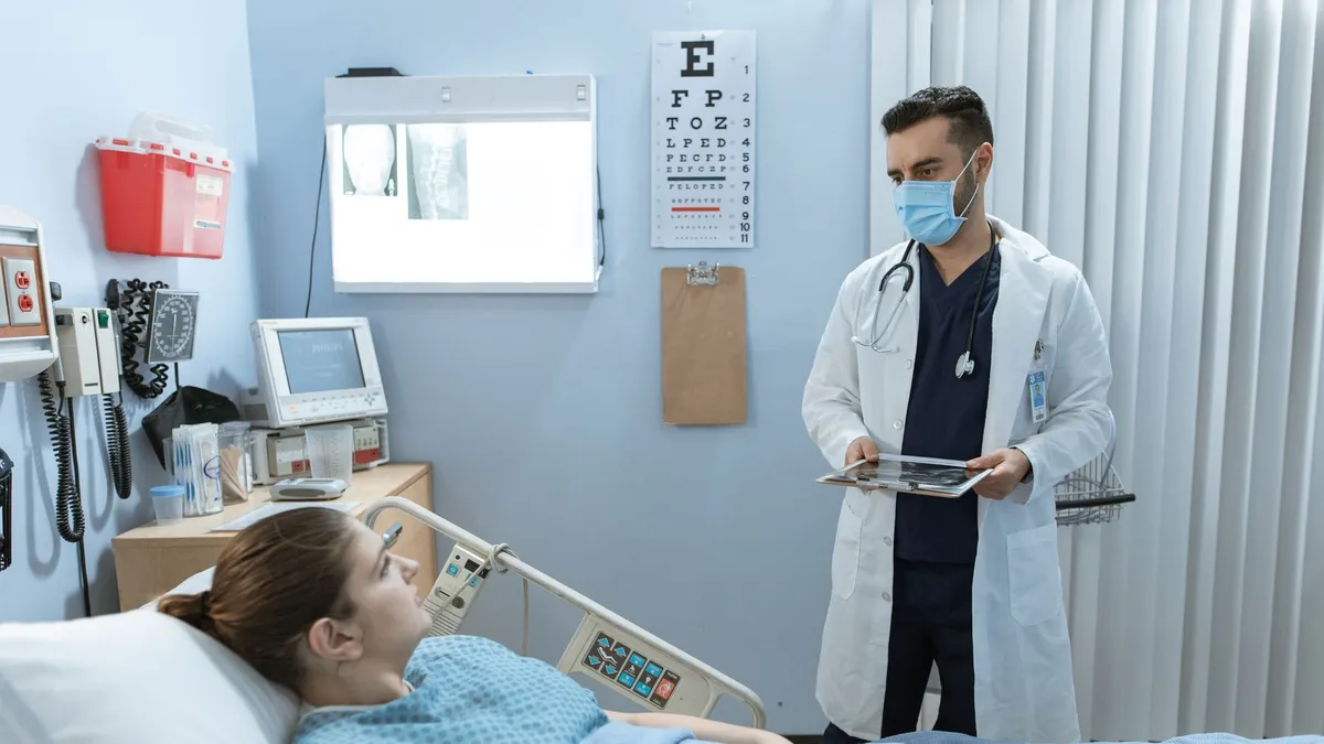 Doctor wearing face mask consulting with a patient in a hospital room, highlighting healthcare safety.