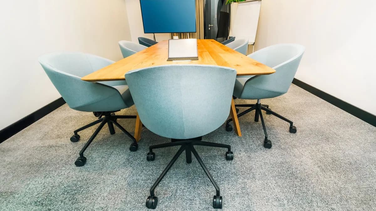 A stylish conference room featuring a triangular table, office chairs, and a TV screen.
