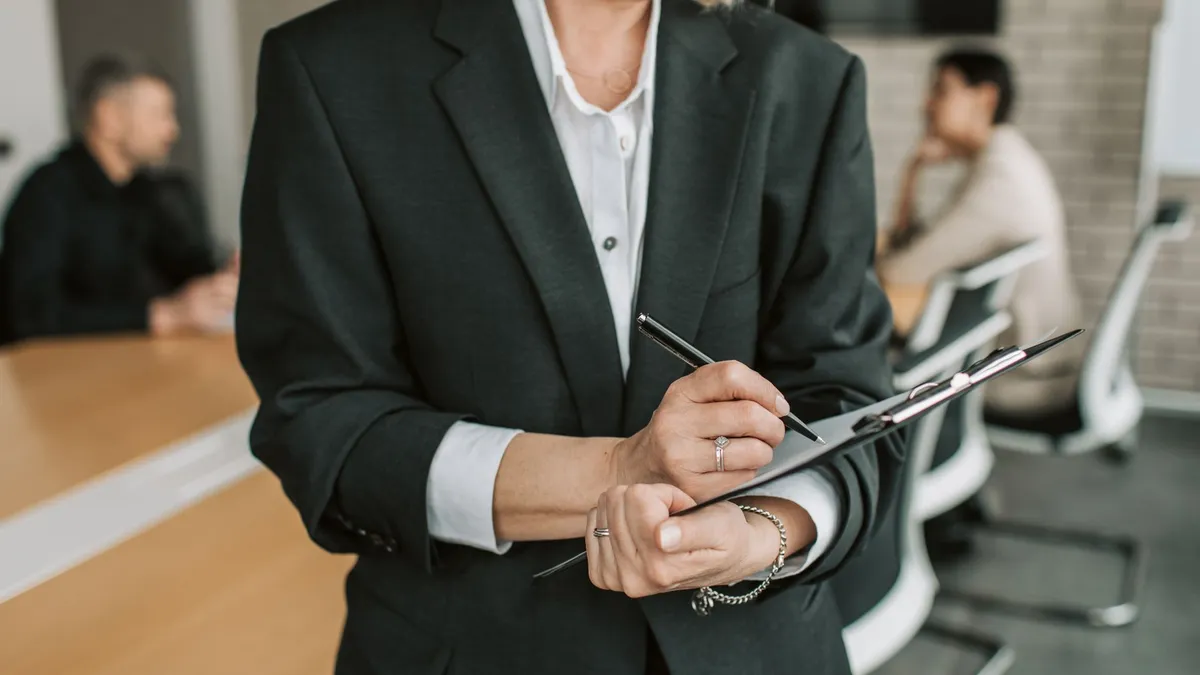 Professional in black suit taking notes during a business meeting.
