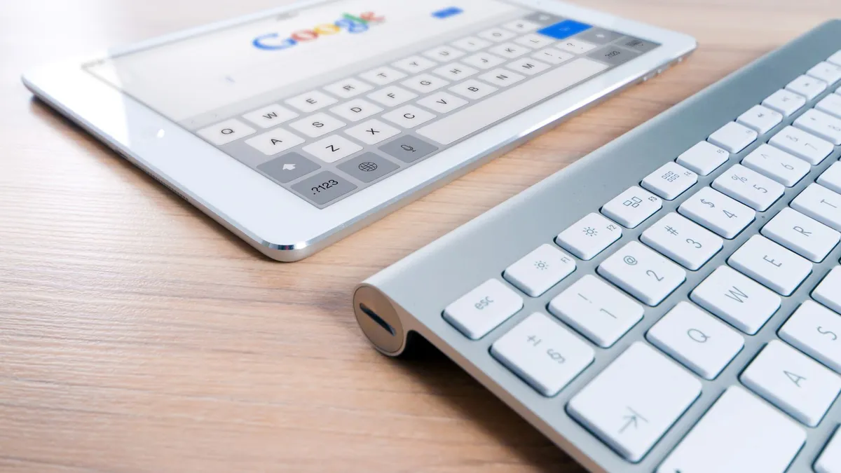 A modern tablet displaying a search engine logo next to a wireless keyboard on a wooden desk.