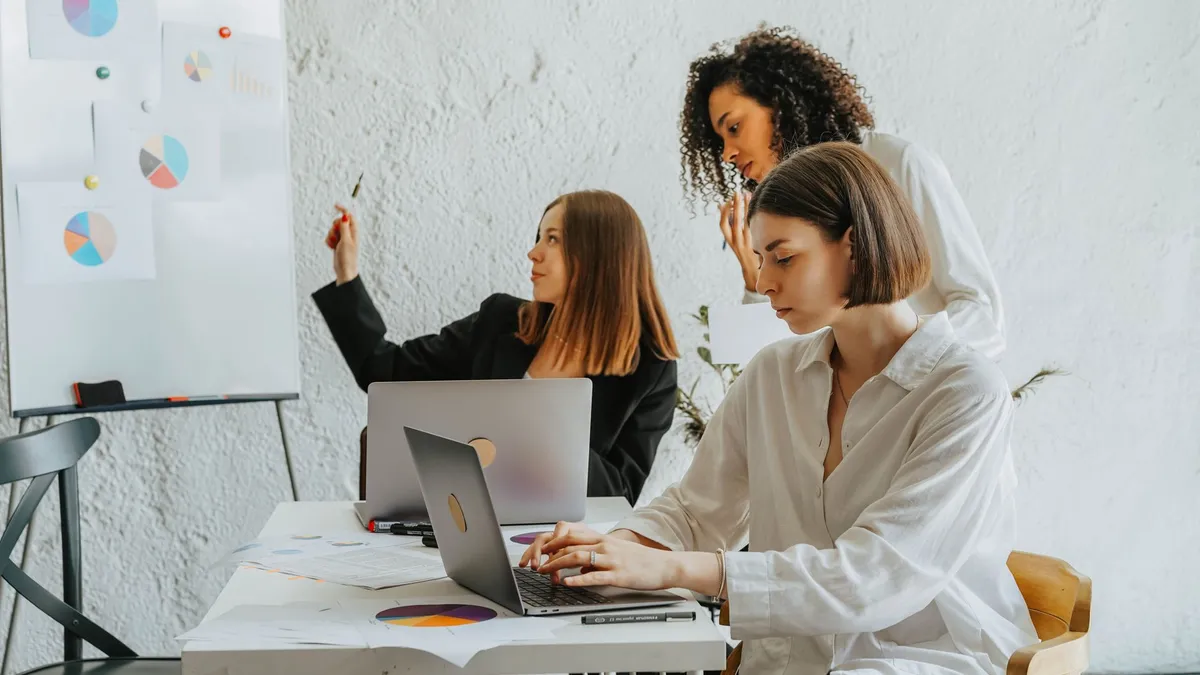 Women working together on a business project with laptops and charts. Collaborative and diverse environment.