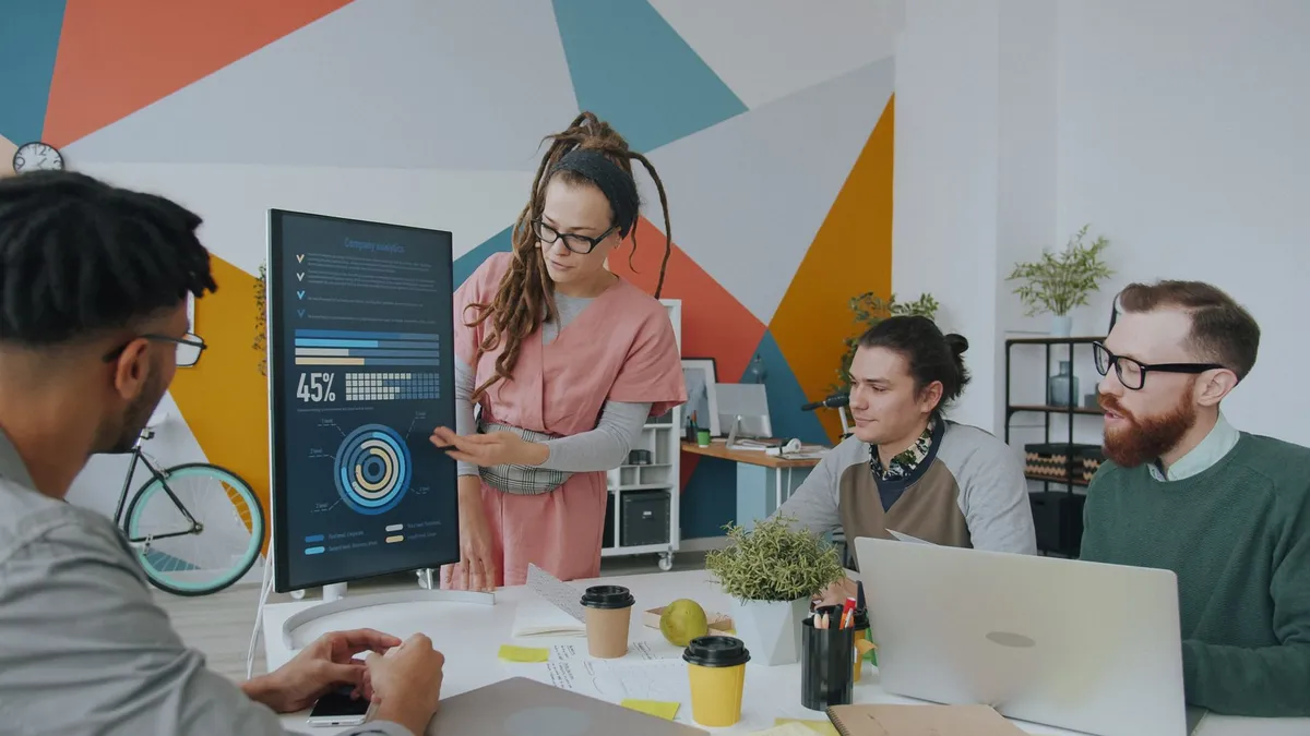 A diverse team discusses analytics displayed on a monitor in a vibrant office setting, promoting collaboration.