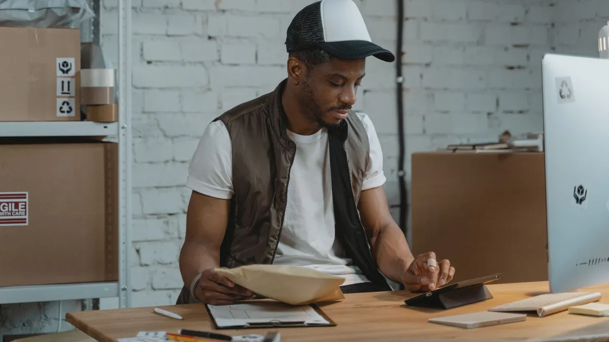 A man in a warehouse managing e-commerce orders and using a tablet for logistics.