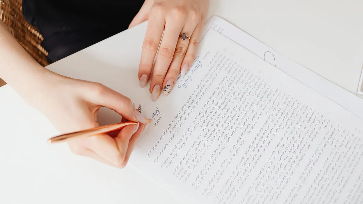 Close-up of woman's hands signing a legal document with elegant nail art using a pen.