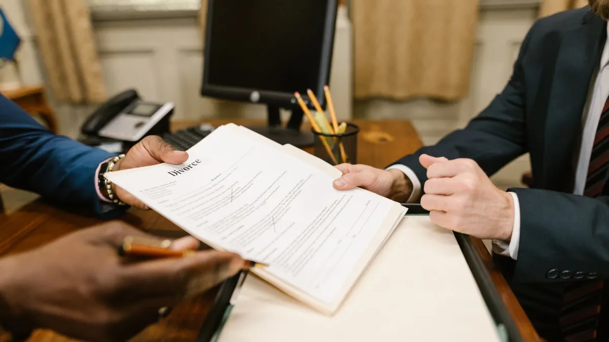Close-up of hands exchanging divorce documents during legal proceedings in office.