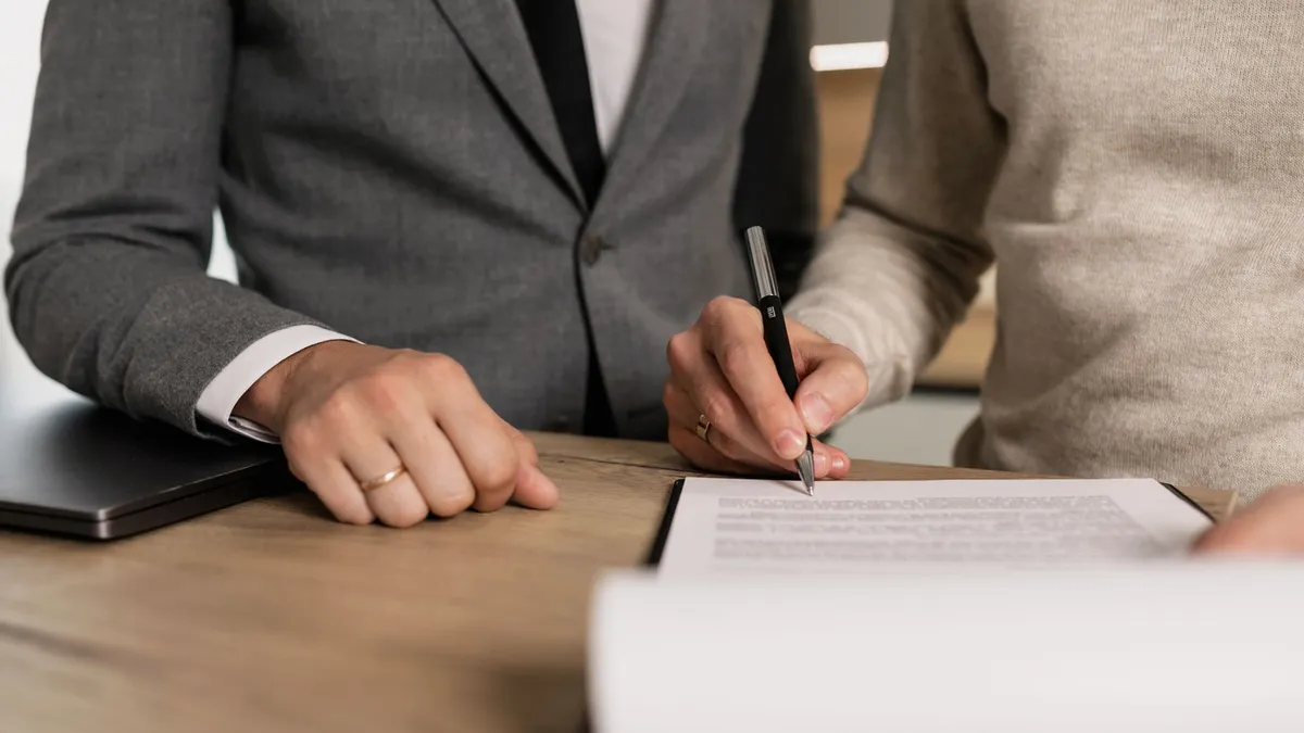 Close-up of businessmen signing documents at a wooden table in an office.