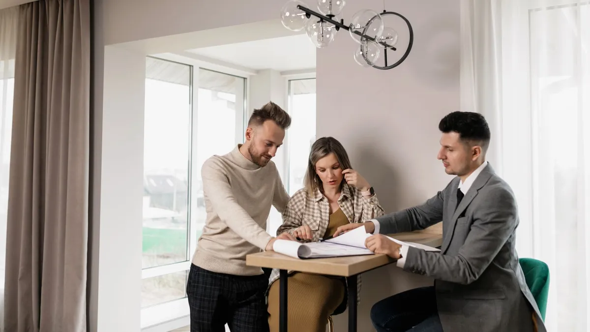 A couple consults with a real estate agent in a modern indoor setting, reviewing property documents.