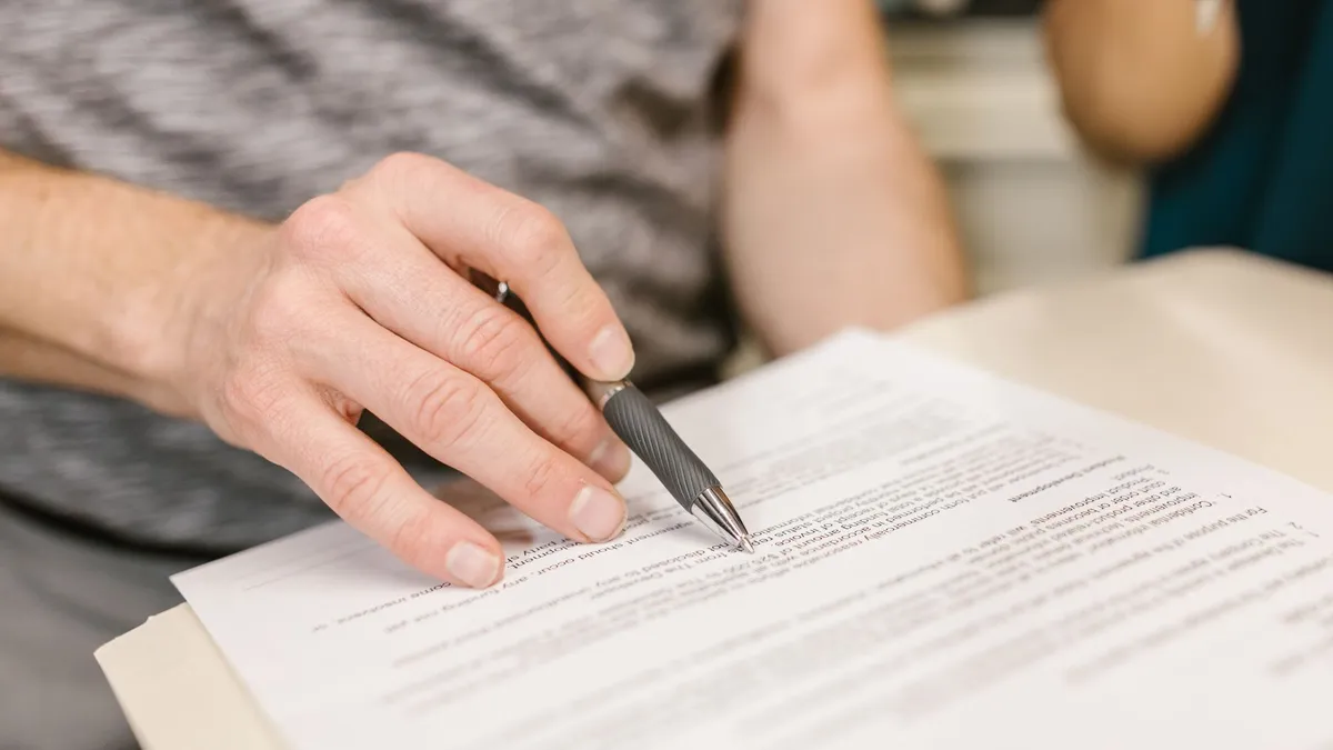 Close-up of a person's hand signing an important legal document with a pen indoors.