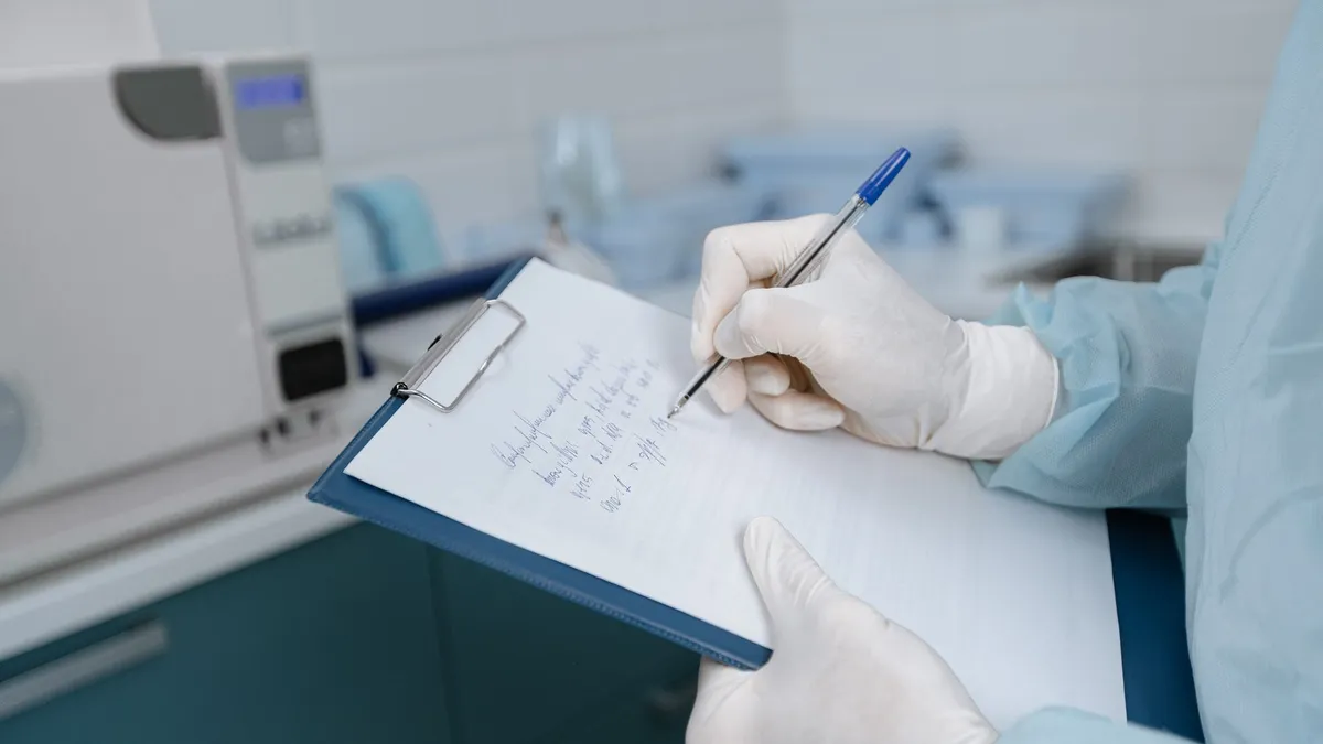 Medical worker in lab coat writing notes in a clinic setting.