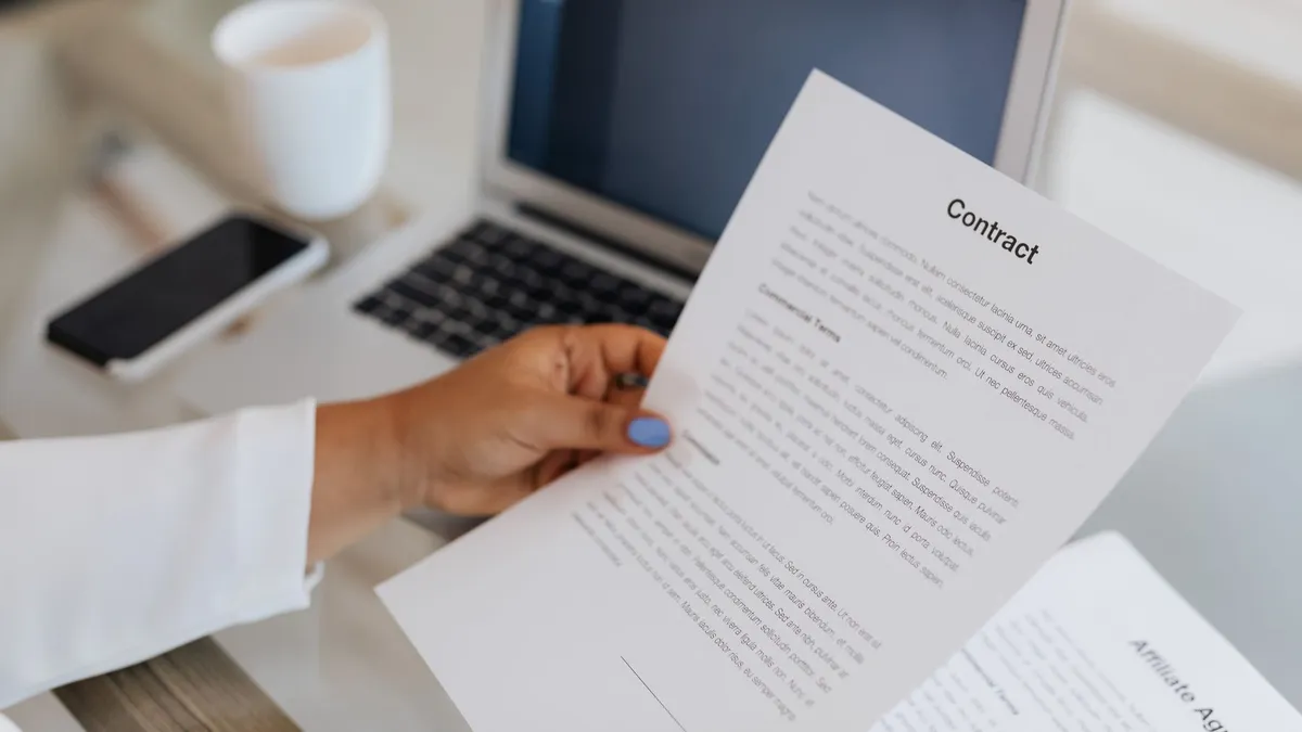 Close-up of a person holding a contract document next to a laptop during a work session.
