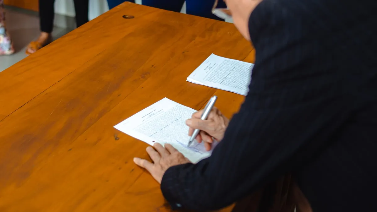 A close-up of a businessman signing official documents at a wooden desk.