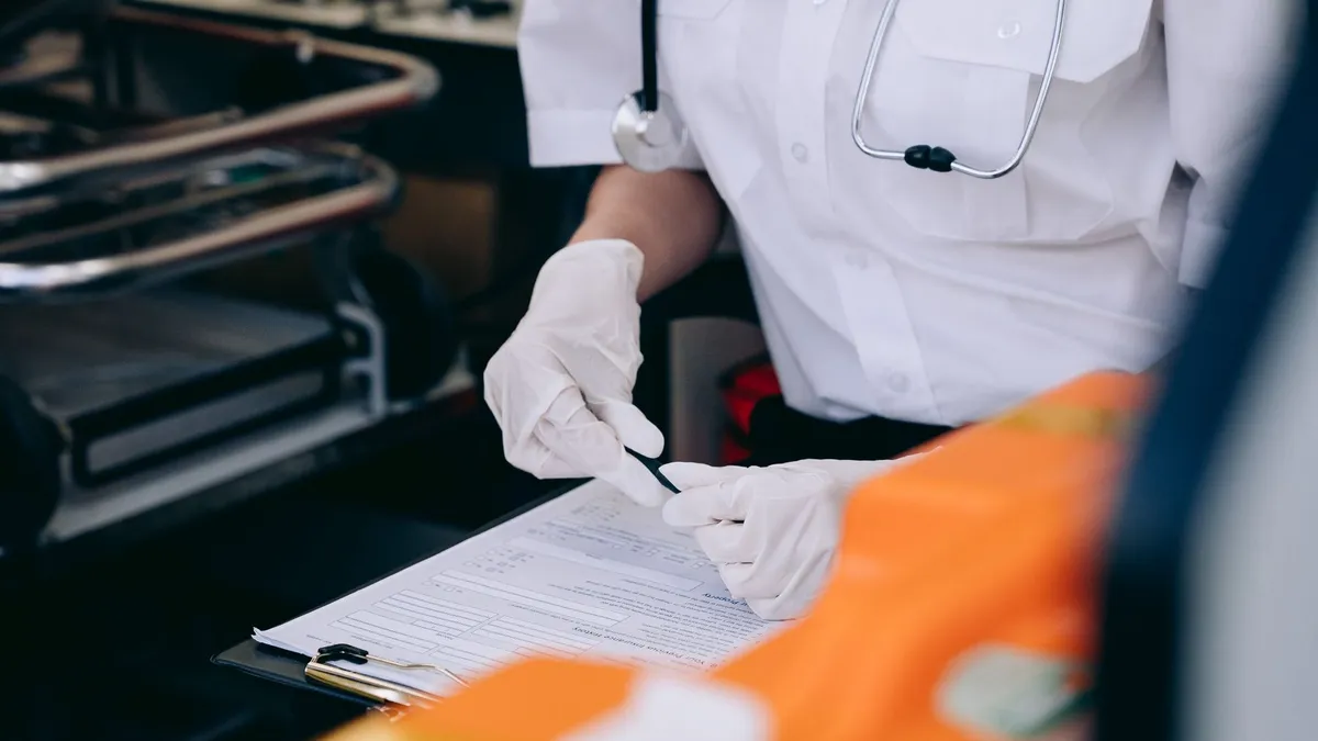 A medic wearing gloves and a stethoscope takes notes inside an ambulance.