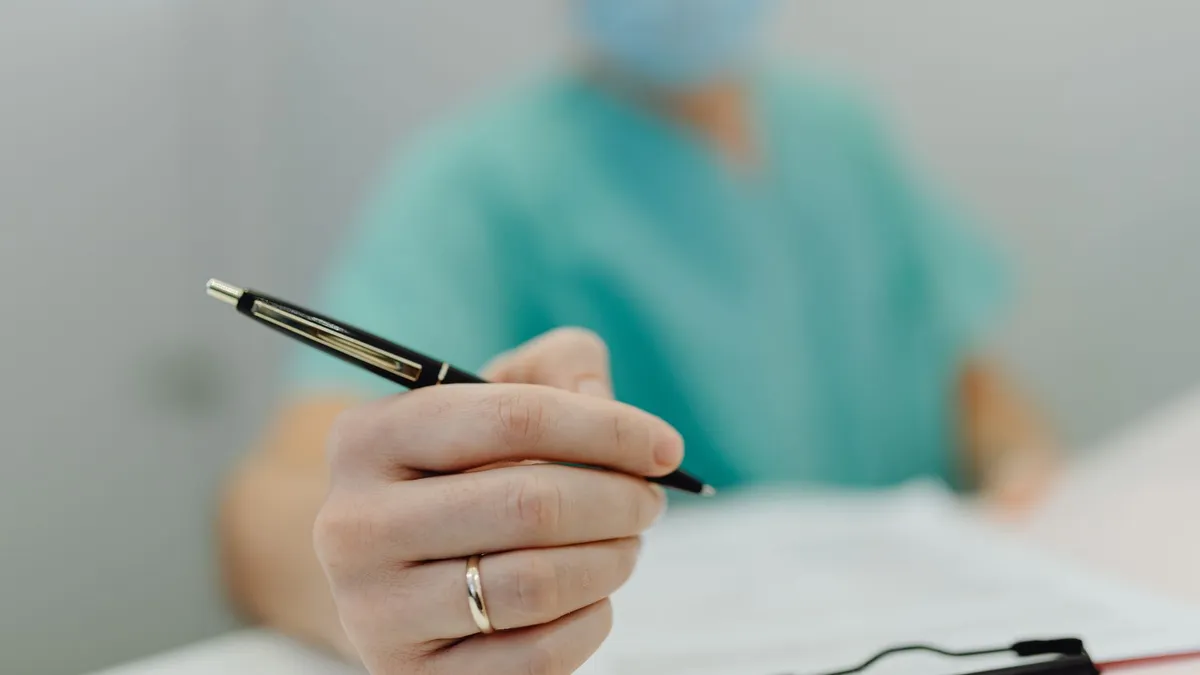 Close-up of a medical professional in scrubs writing with a pen, showing focus on hand and pen.