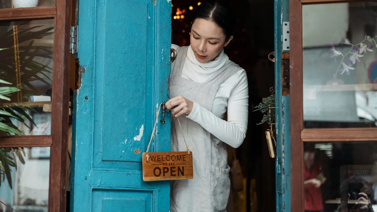A woman adjusts an open sign on a blue wooden door of a cafe inviting customers inside.