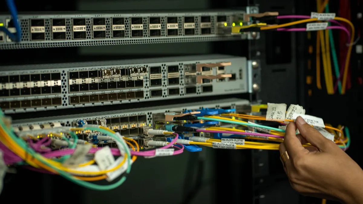 A hand managing fiber optic cables in a server room, showcasing modern connectivity.