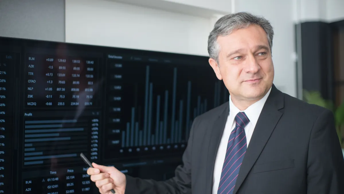 Professional man in suit reviewing financial charts on monitor, showcasing stock market trends.
