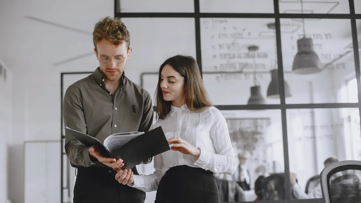 Two professionals discuss documents in a modern office environment.