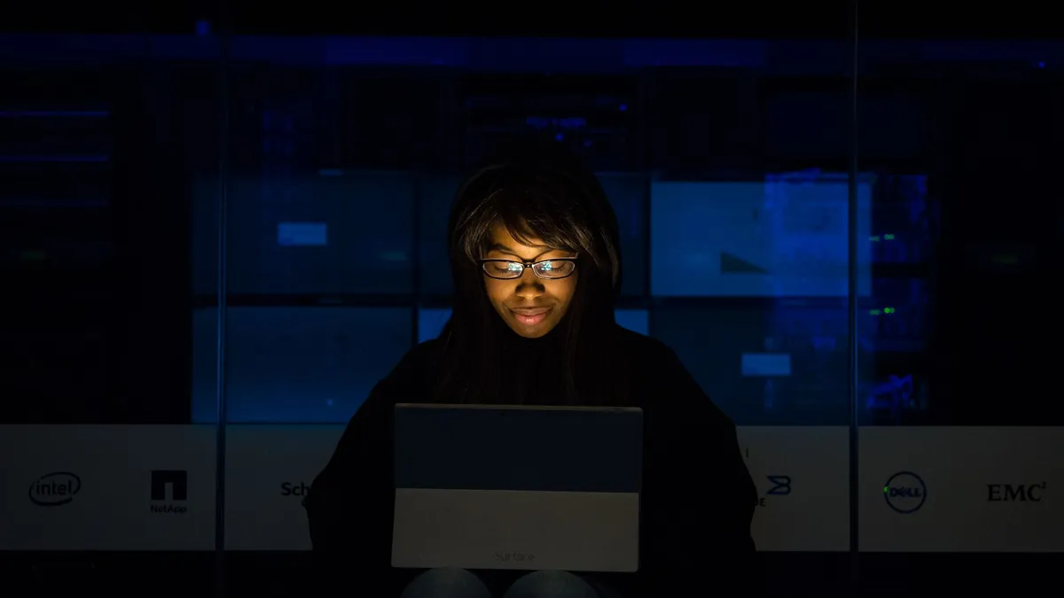 A woman uses her laptop in a dimly lit server room, focusing on technology and work.