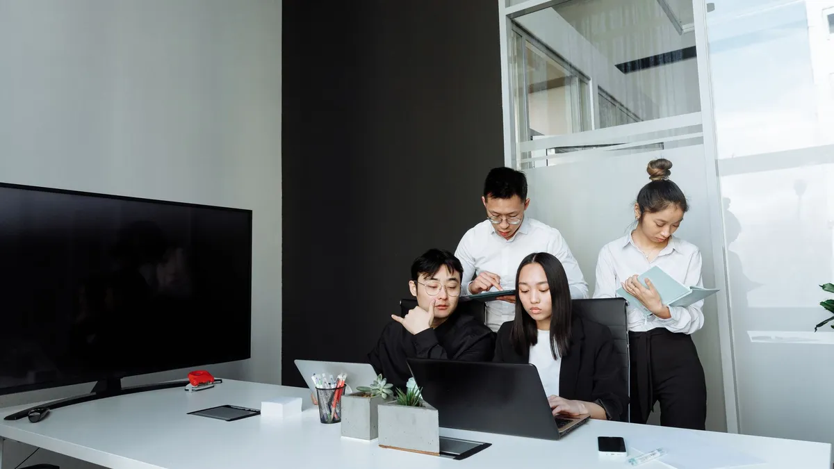 Team of young professionals collaborating in a modern office setting, engaging with laptops and documents.
