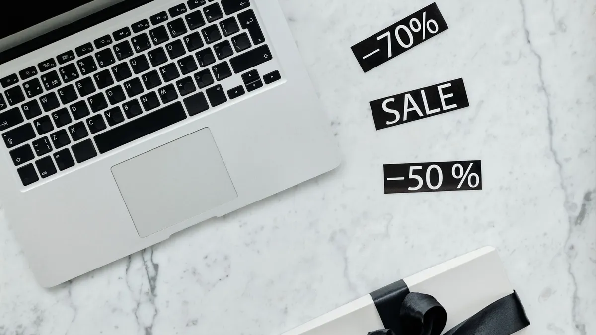 Marble workspace with a laptop, gift box, and sale tags offering discounts.
