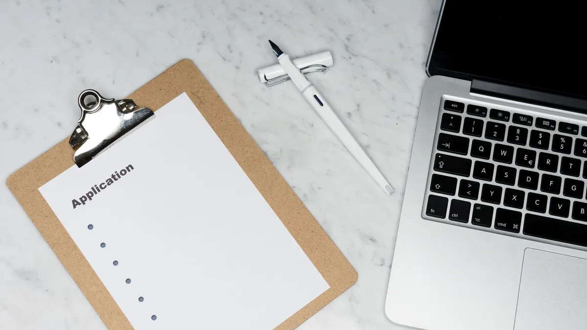 A clean and organized office desk setup featuring a laptop, clipboard with application form, and pen.