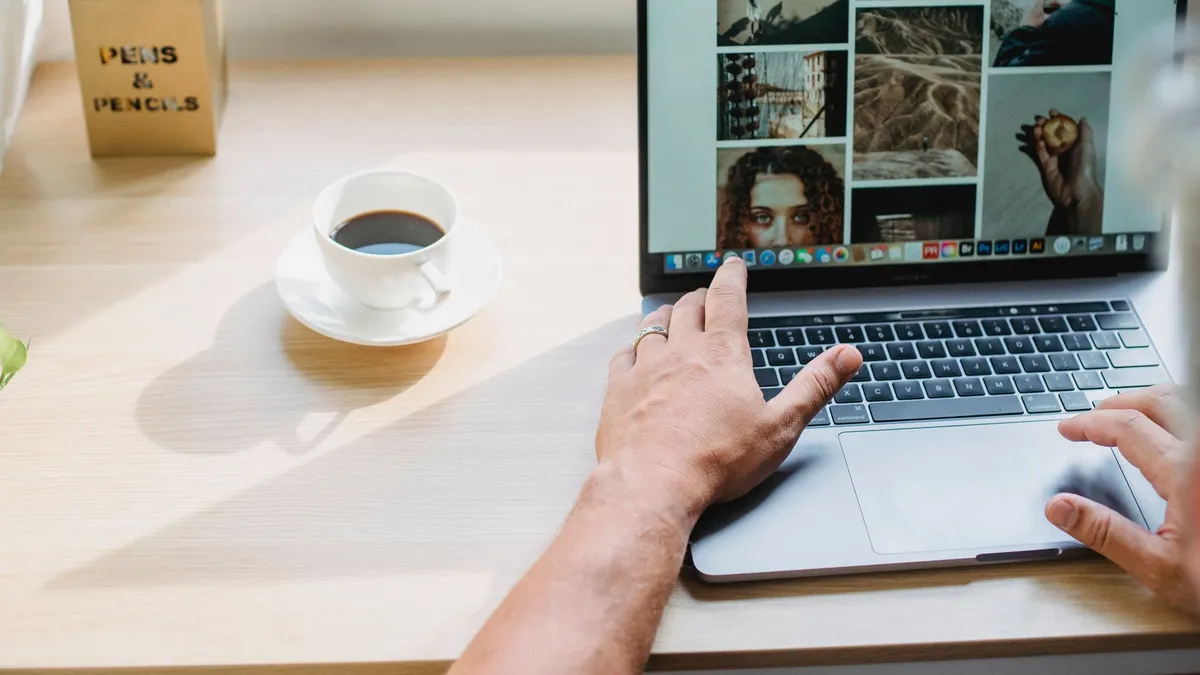 Crop anonymous male searching photos on internet using netbook while drinking coffee at table