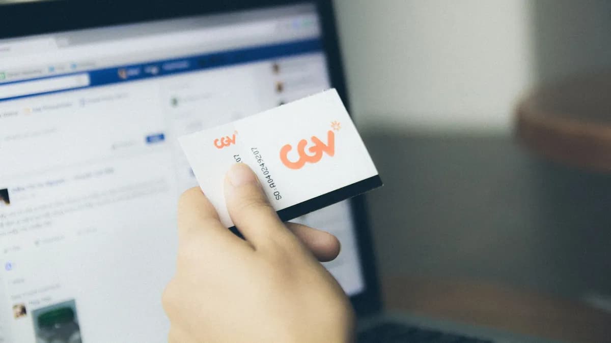 Close-up of a hand holding a card near an active laptop screen, indoors.