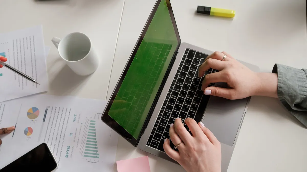 Modern office desk setup with a laptop, papers, and hands typing.