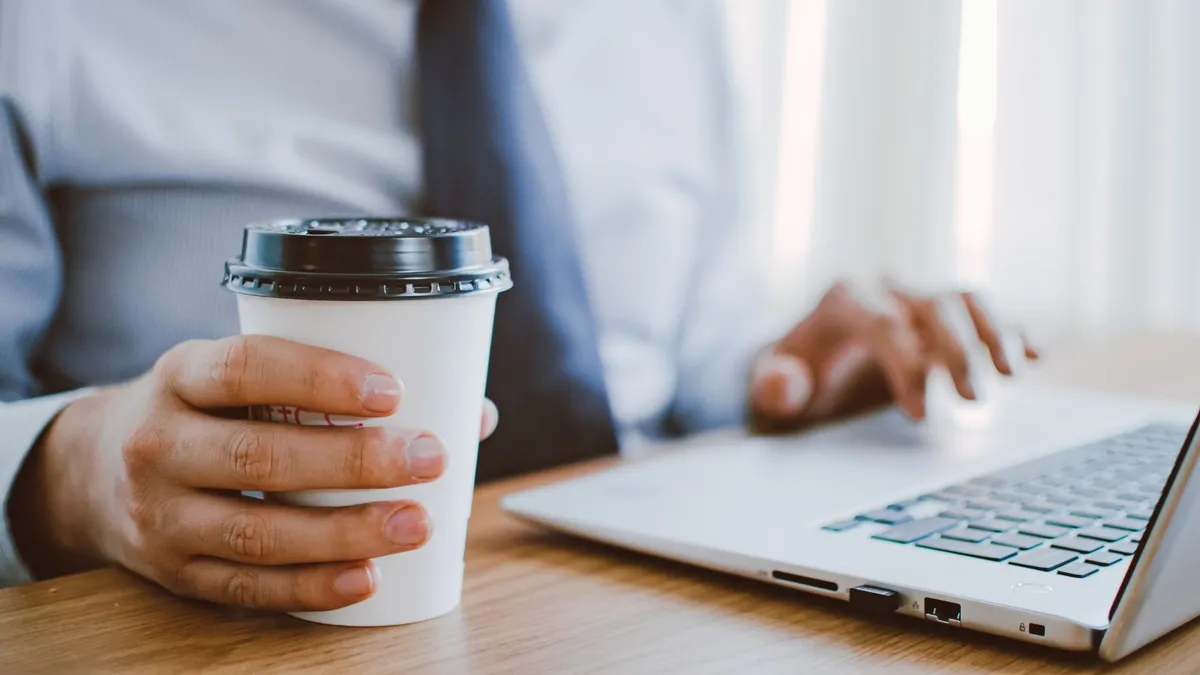 Business professional working remotely, enjoying coffee while using a laptop indoors.