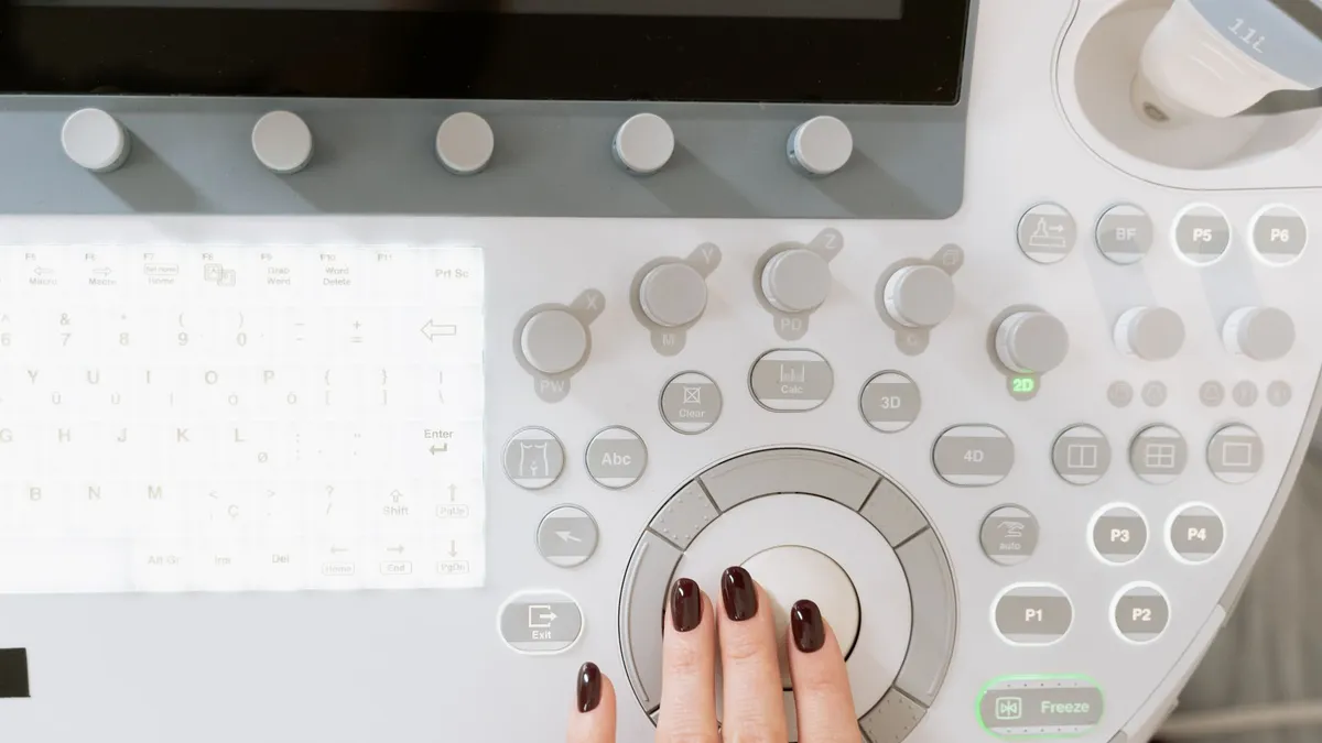 Hand operating a high-tech ultrasound control panel in a medical facility.