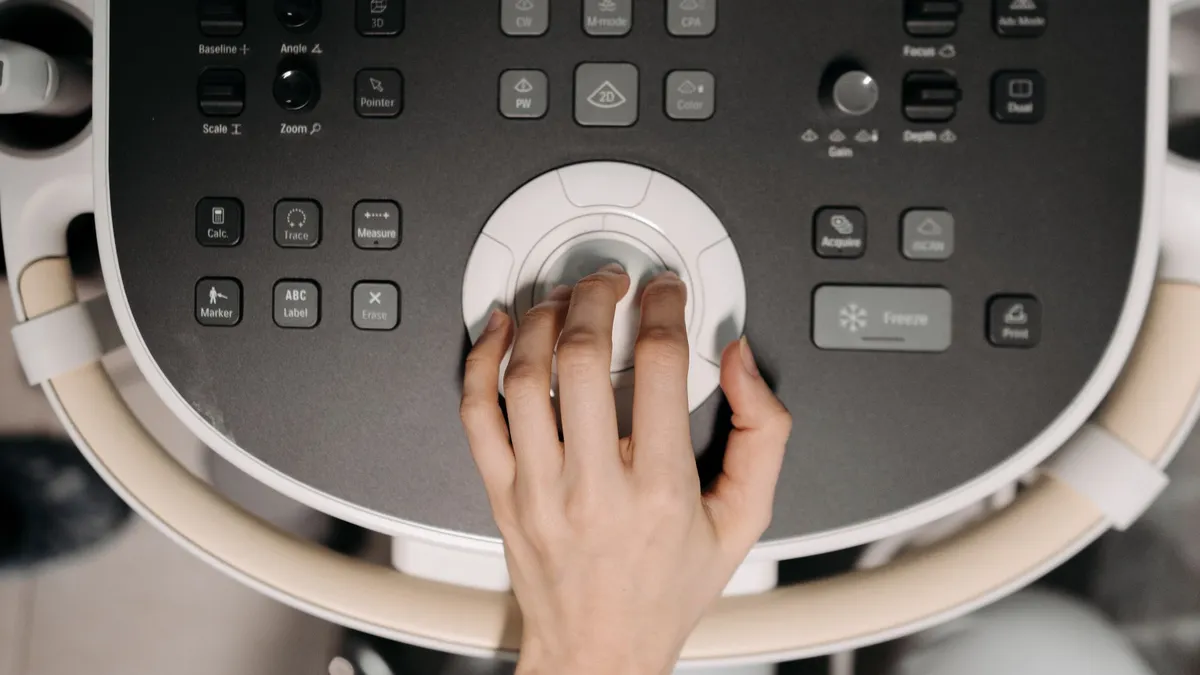 Close-up of hand operating ultrasound machine, illustrating medical technology usage.