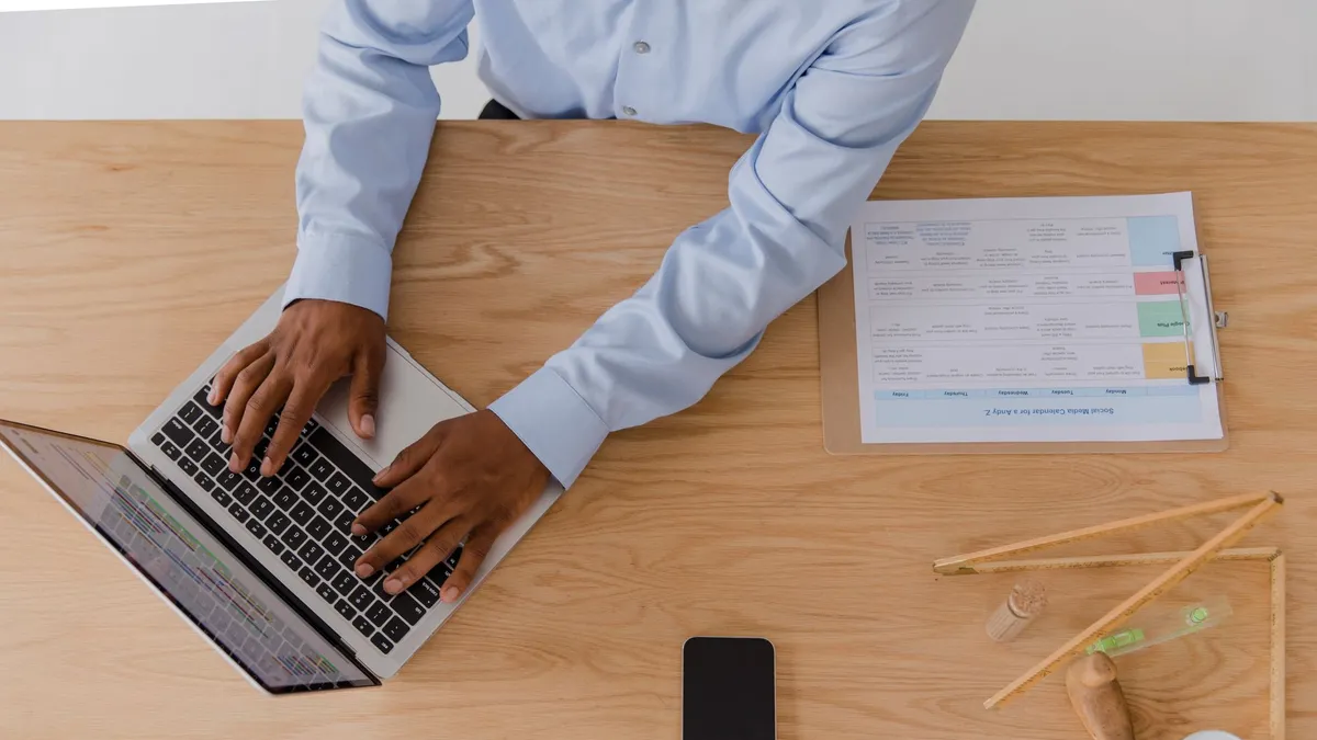 Top-down view of a man in business attire working on a laptop at a desk.