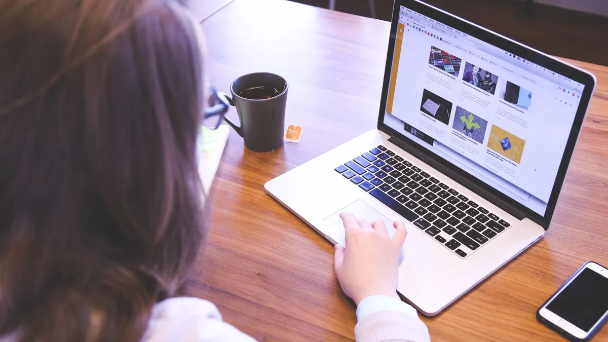 Person browsing the web on a MacBook at a wooden desk with a smartphone.