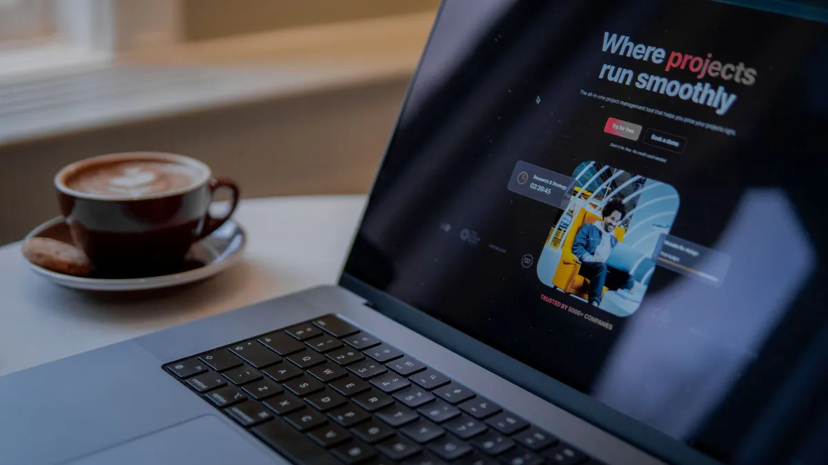 A laptop displaying a project management app sits on a table with a cozy cup of cappuccino in Amsterdam.