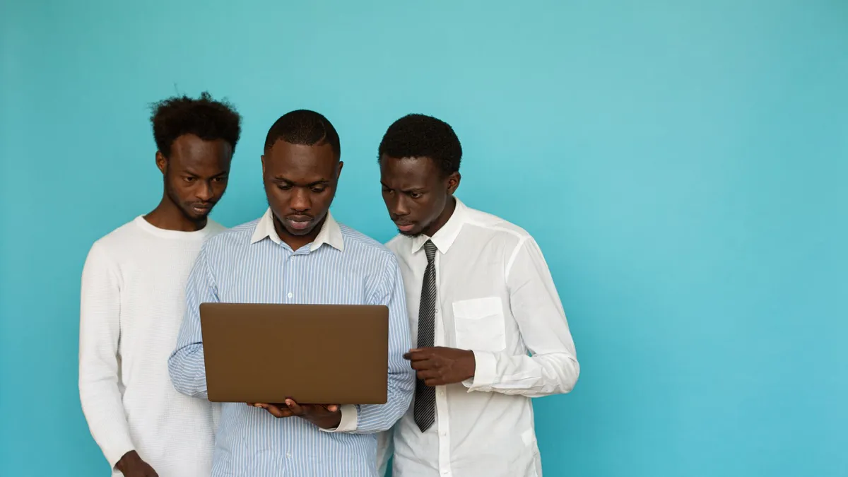 Three men collaborating on a laptop against a teal background, symbolizing teamwork.