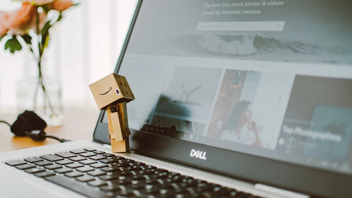 A small toy figure stands on a laptop keyboard with flowers in the background.