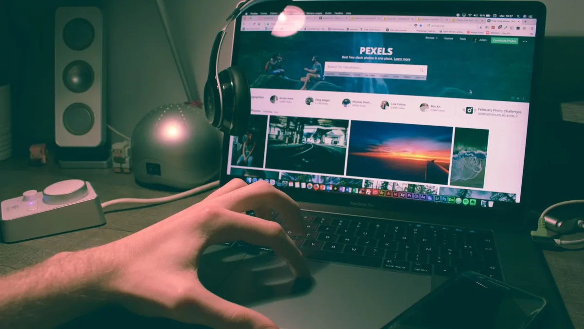 Person browsing Pexels on a laptop with headphones and smartphone nearby.