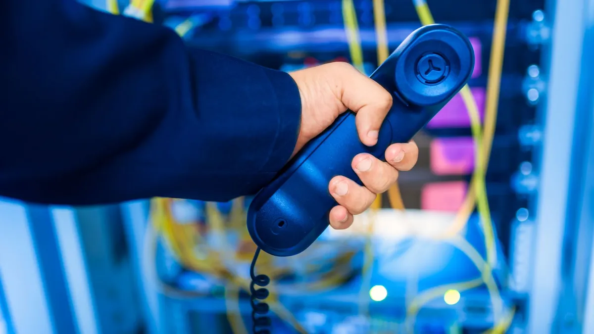 Close-up of a hand holding a telephone receiver in a server room emphasizing technology.