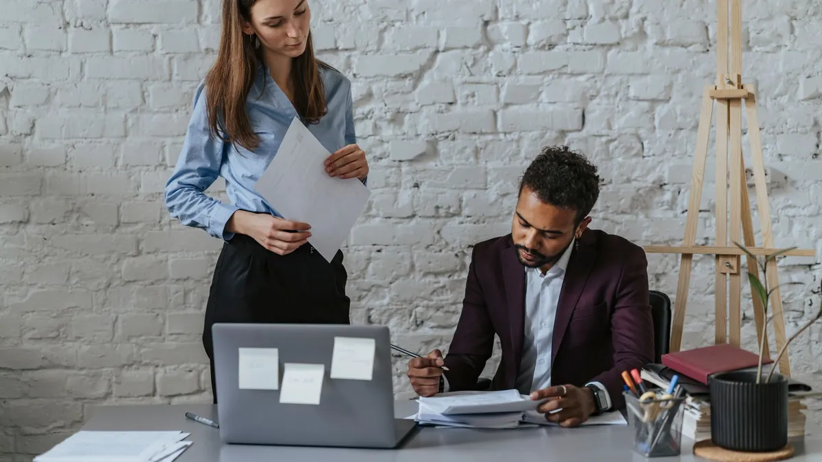 Two professionals in an office discussing documents while working together. Ideal for business themes.