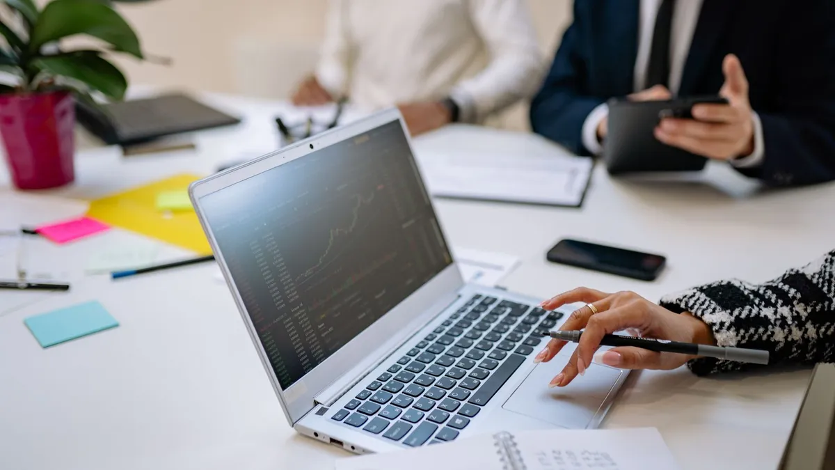 Professionals analyze financial data on laptop during office meeting.