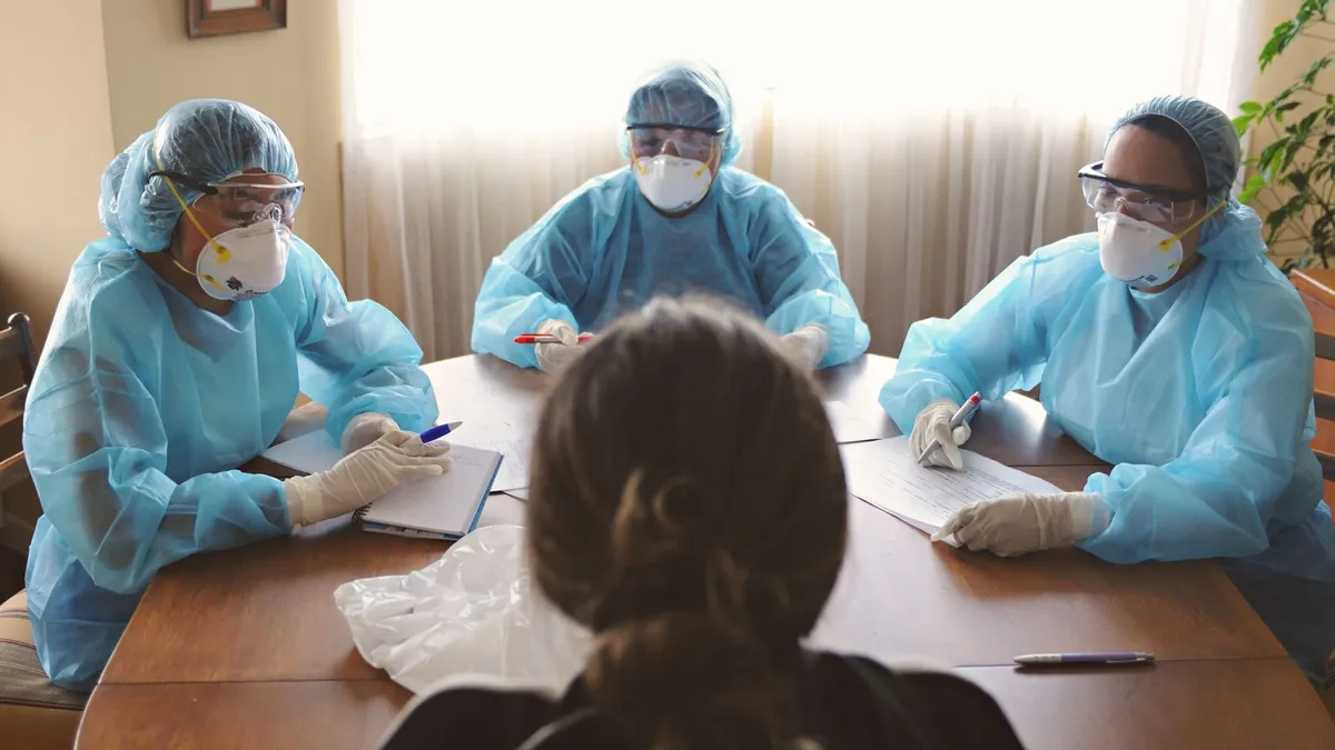 Three healthcare professionals in PPE discuss patient care indoors.