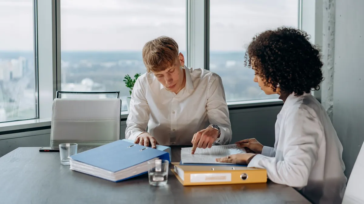 Two professionals reviewing documents in a high-rise office with city views.