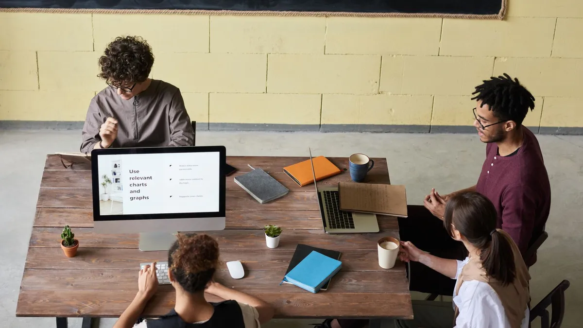 Four diverse colleagues engaged in a team meeting, working on laptops with coffee and notes, fostering collaboration.