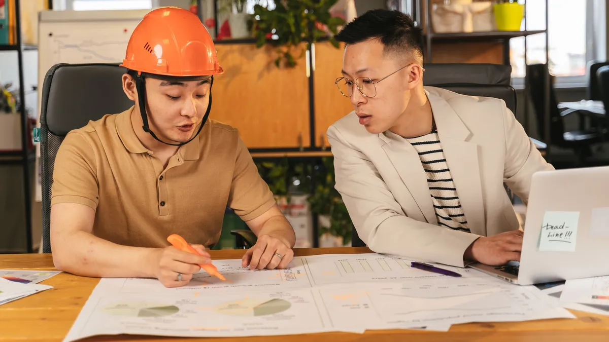 Two men collaborating on project plans in an office setting, reviewing documents on a table.