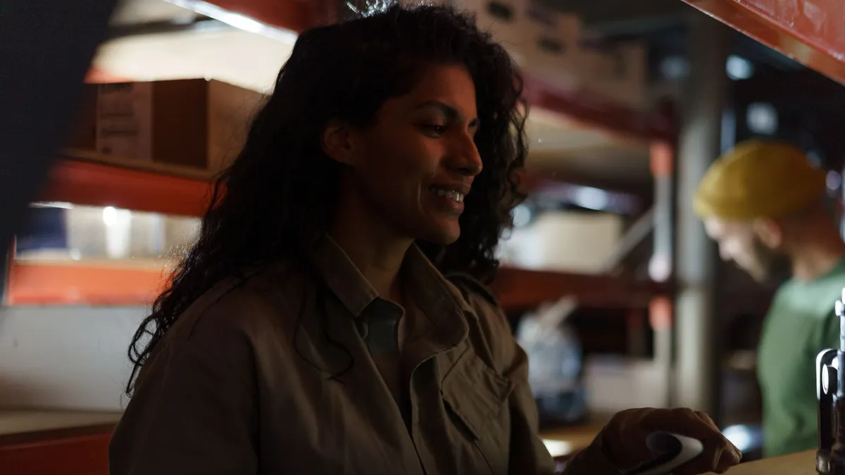 Smiling female worker examines inventory in a dimly lit warehouse.