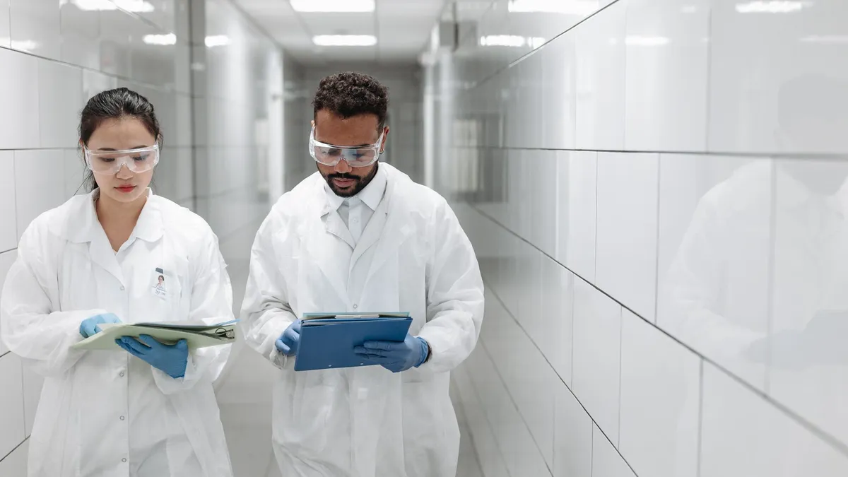 Two researchers in lab coats review documents in a clinical laboratory hallway.